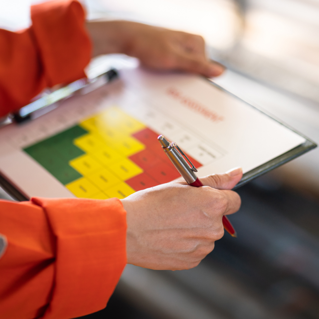 Image description: A close-up photograph of a clipboard, held by two arms with orange sleeves. The clipboard contains a financial report consisting of graphs, charts, and numbers.