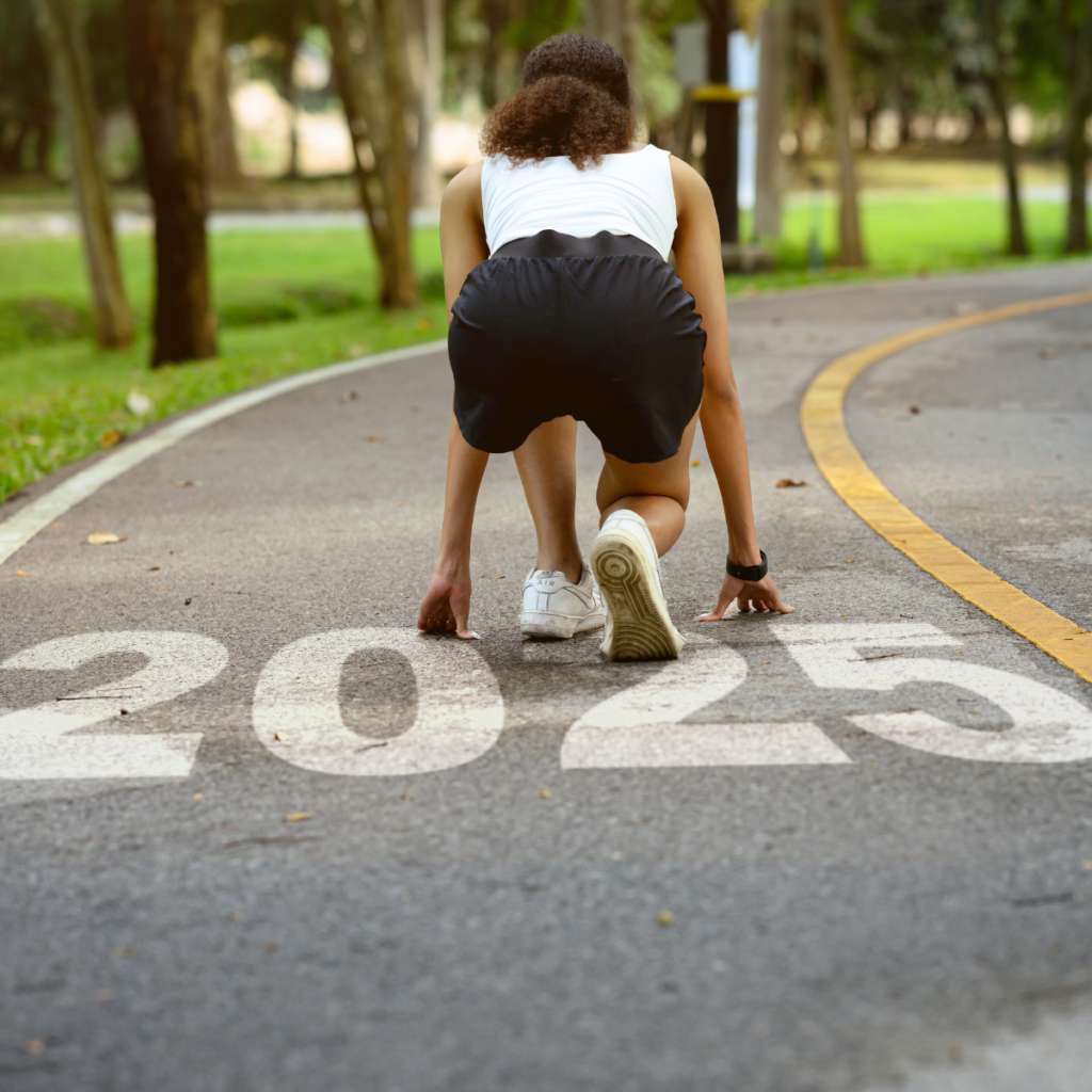 A woman in a starting position for a running race, crouching low on a track. The number '2025' is prominently displayed on the asphalt beneath her, indicating the year of the event.