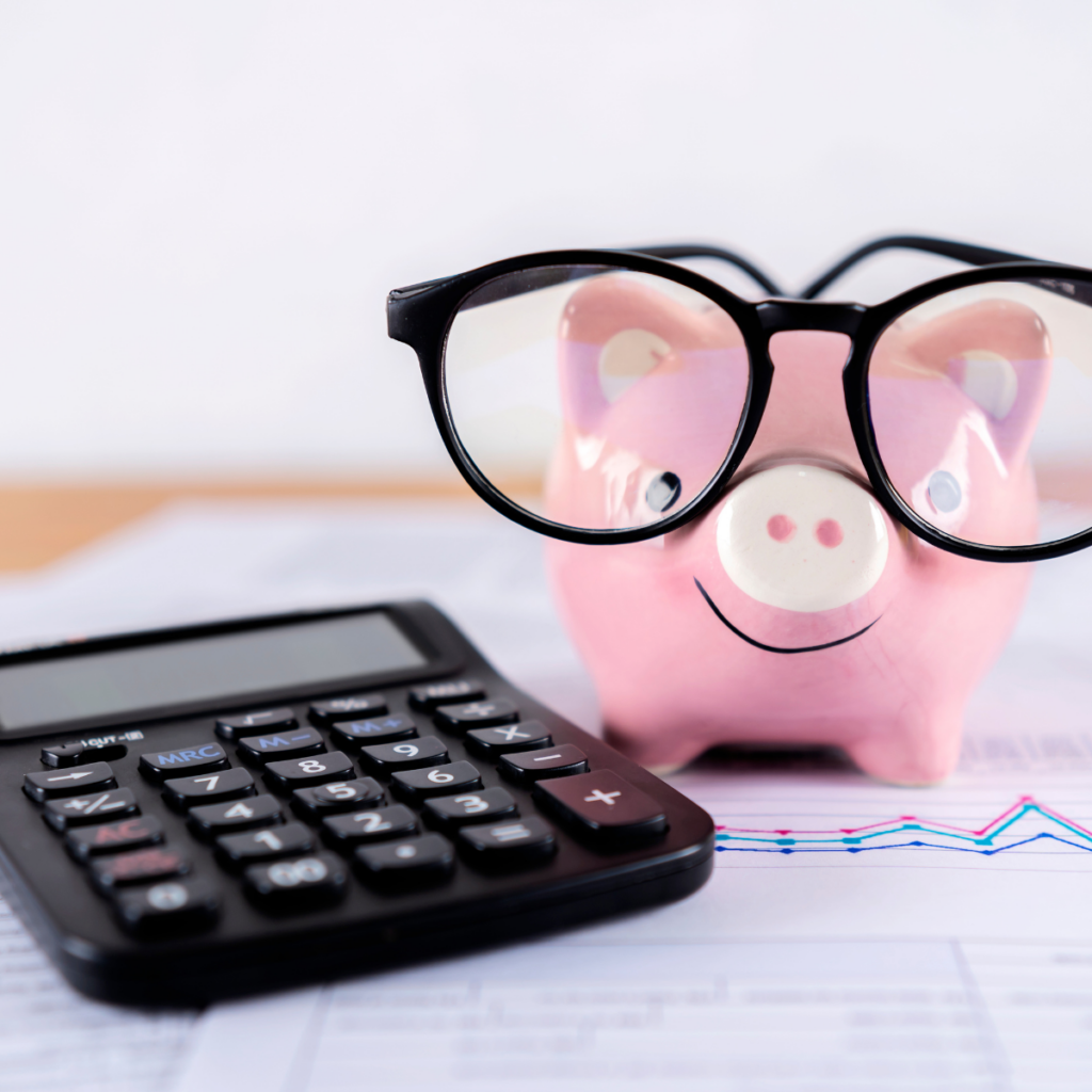 A pink piggy bank wearing a pair of oversized black-framed glasses, positioned next to a calculator, all resting on a pile of financial paperwork.